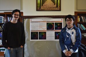 Two students stand in front of their research poster. The poster contains colorful fractal patterns on a black background. 